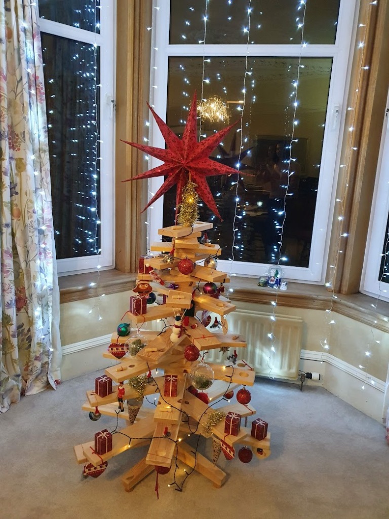 Wooden Christmas tree decorated with ornaments, lights, and a big red start on the top.